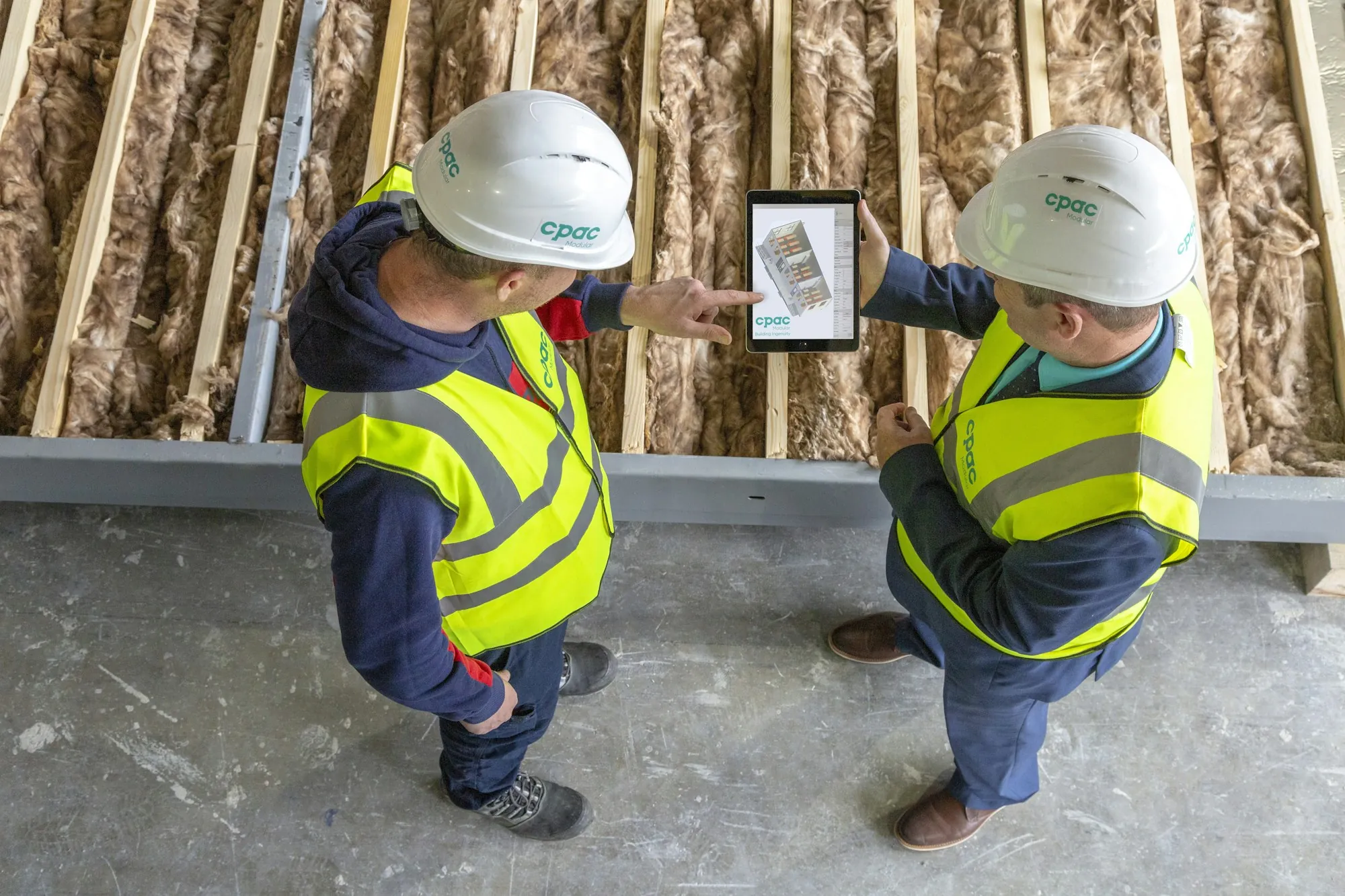 Two workers in hard hats reviewing plans on a tablet